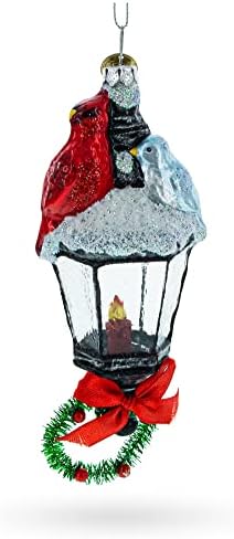 קרדינל אדום יושב על קישוט חג המולד של זכוכית פנס מכוסה שלג